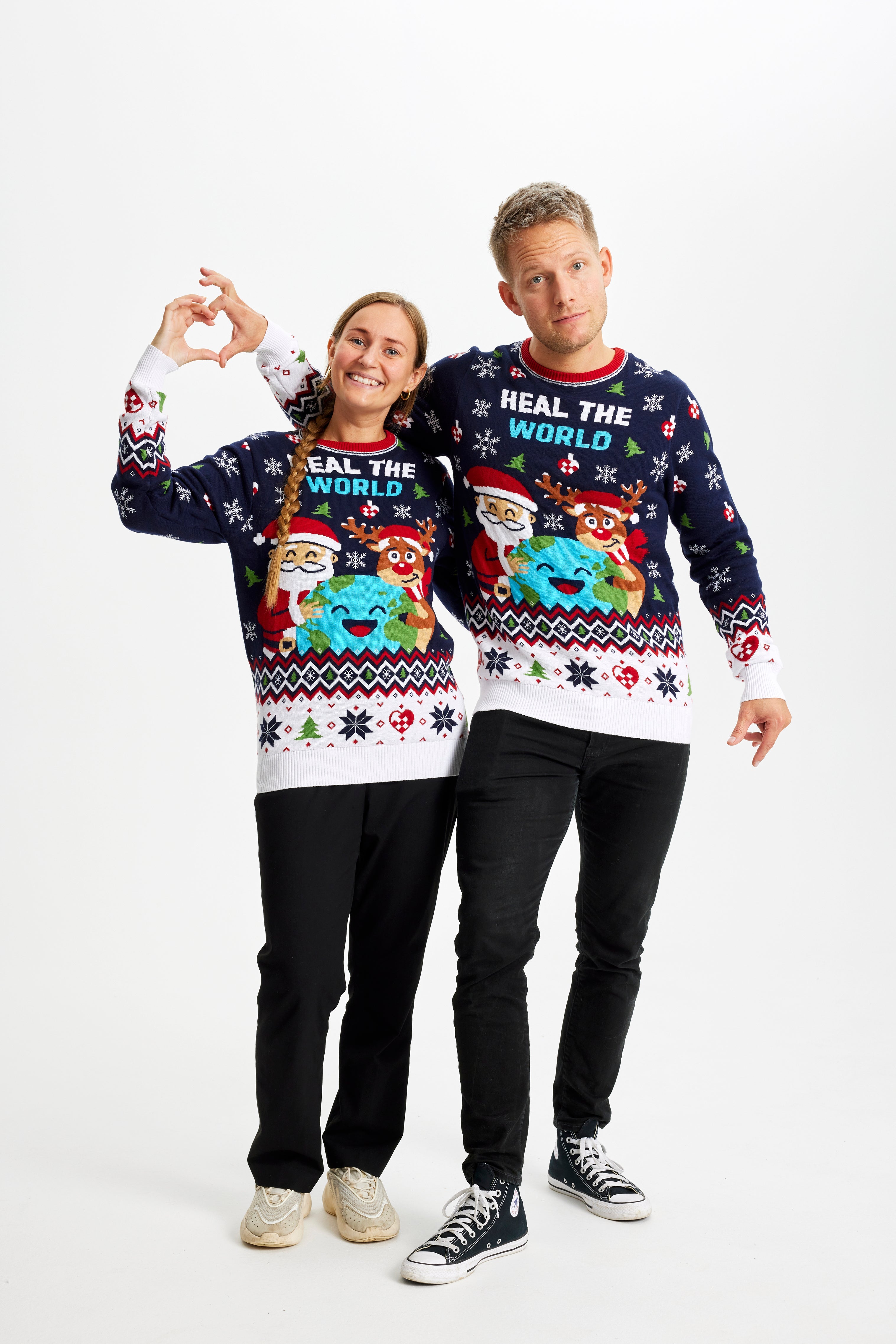 En kvinde og en mand viser hjertetegn med deres hænder og er iført en julesweater.